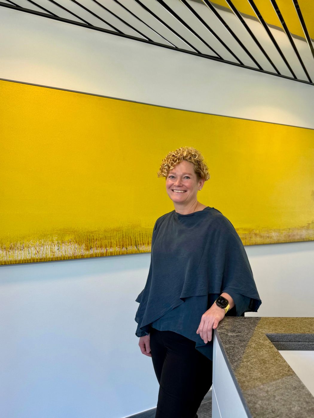 Angela M. Schmidt, smiling, in front of a large yellow painting.